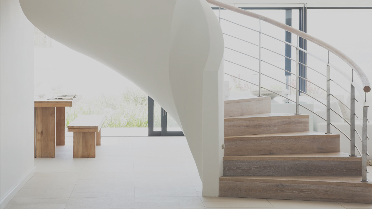 A curved staircase in a home, with a railing on the right of the stairs and a white partitioning wall on the left